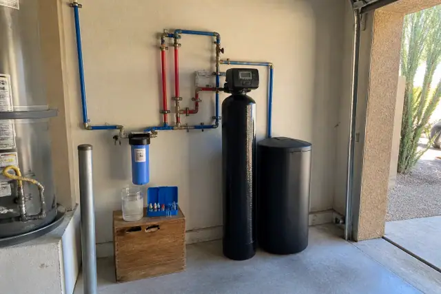 Water softener system installed in a residential garage in Mesa, AZ, with a water testing kit on a wooden crate.