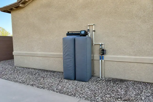 Water softener with an insulated cover and neat plumbing installed against an exterior wall in Mesa, AZ.