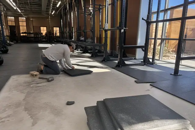 Technician installing rubber flooring in a fitness center free weight zone in Phoenix, AZ.