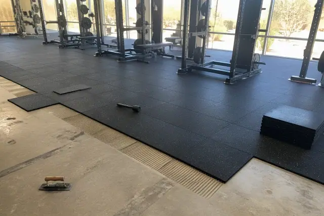 Technician installing heavy-duty rubber floor tiles in a Phoenix, AZ fitness center free weight zone.
