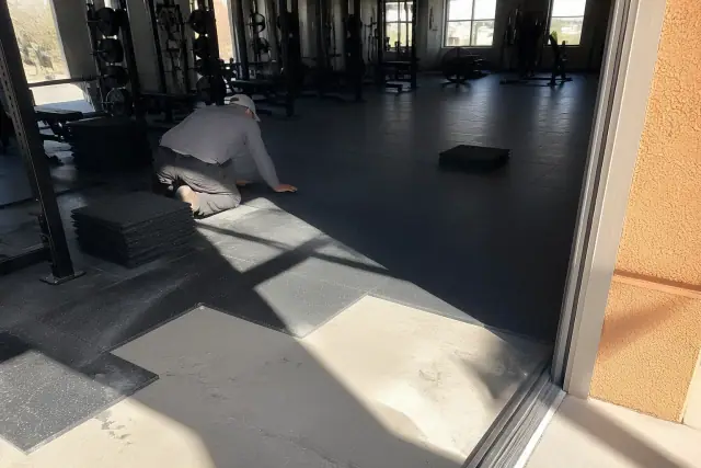 Technician installing heavy-duty rubber gym flooring tiles on a concrete slab in Phoenix, AZ.