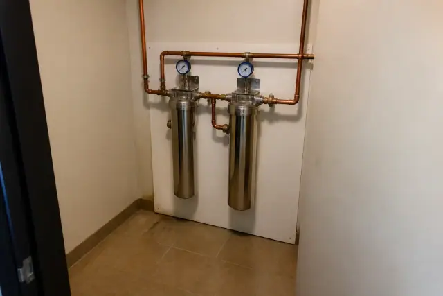 Commercial carbon filtration system with stainless steel housings and copper pipes in a Tempe, AZ office utility closet.