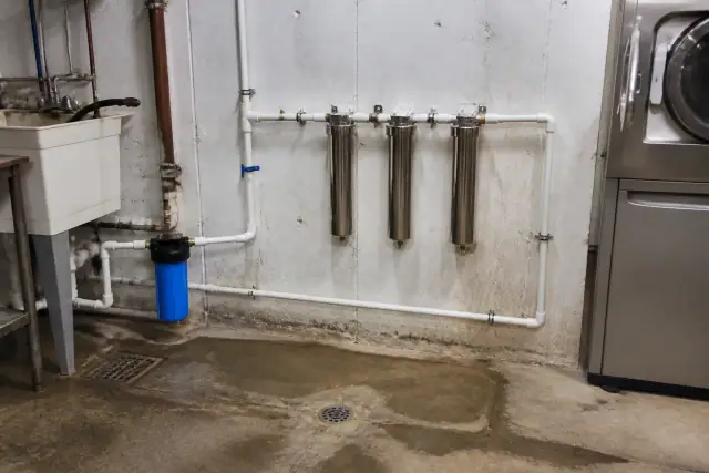Stainless steel water filter housings and white piping in a utility room in Tempe, AZ.