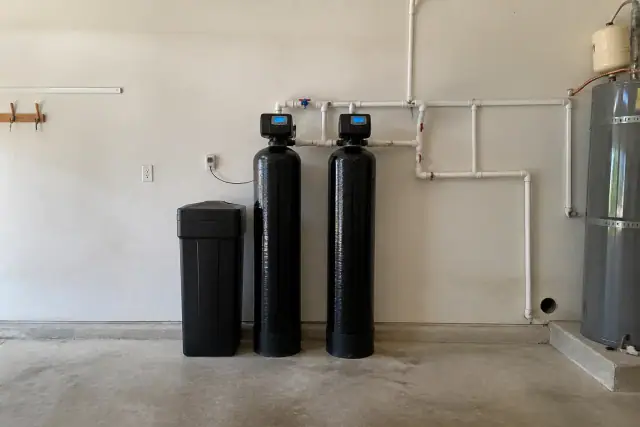 Commercial water softener system with two resin tanks and plumbing installed in a garage in Tempe, AZ.