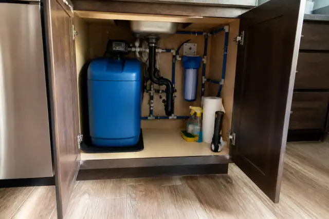 A newly serviced water filtration system with blue softener and clean piping under a kitchen sink in Scottsdale, AZ.