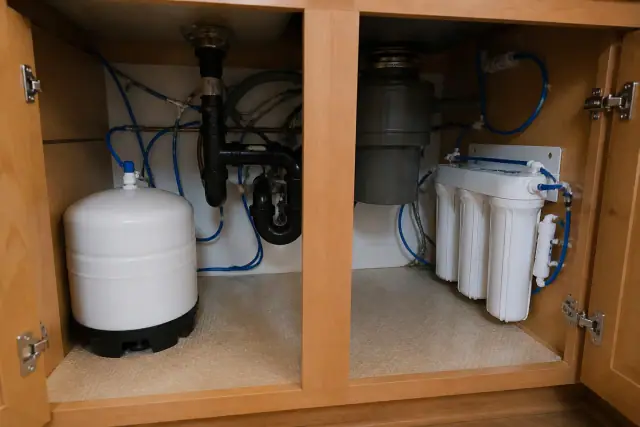 Newly installed water softener and filtration system with blue tubing under a kitchen sink in Surprise, AZ.