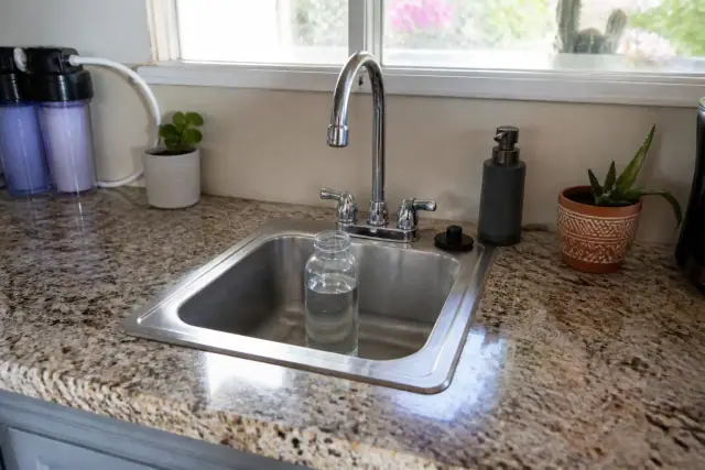 Clear glass water sample bottle under a chrome kitchen faucet on a granite countertop in a home in Tempe, AZ.