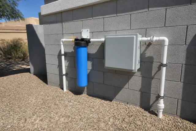 Commercial water filtration system with PVC piping mounted on a grey cinder block wall in Tempe, AZ.