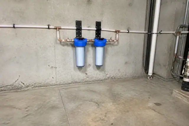 Professional whole-house water filtration system with PEX piping installed on a concrete wall in Tempe, AZ.