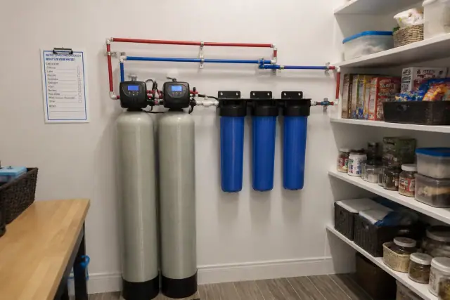 Whole-house water filtration system with blue housings and tanks installed in a pantry in Tempe, AZ.