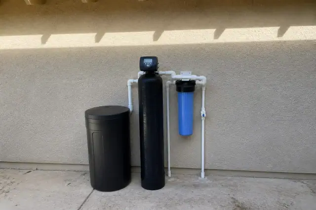 Water softener installation with a brine tank and filtration unit against a stucco wall in Glendale, AZ.