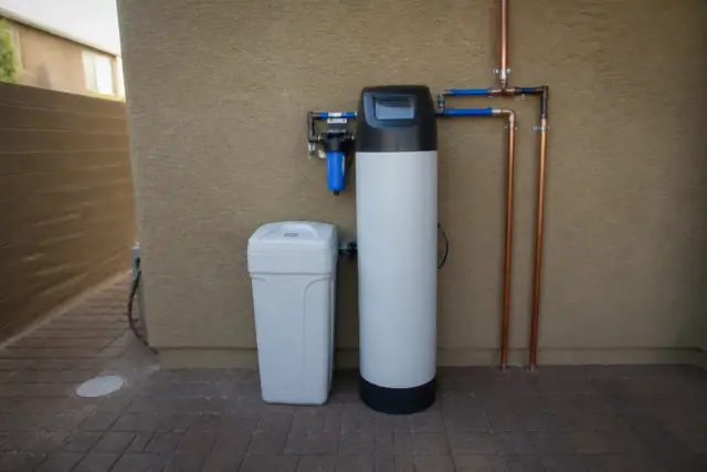 Water softener unit with a white brine tank and copper piping installed on a stucco wall in Avondale, AZ.