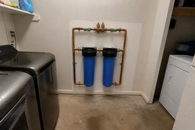 Whole house water filtration system with blue housings and copper pipes installed in a laundry room in Tempe, AZ.