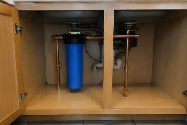 Whole-house water filtration system with blue filter and copper pipes installed under a kitchen sink in Tempe, AZ.