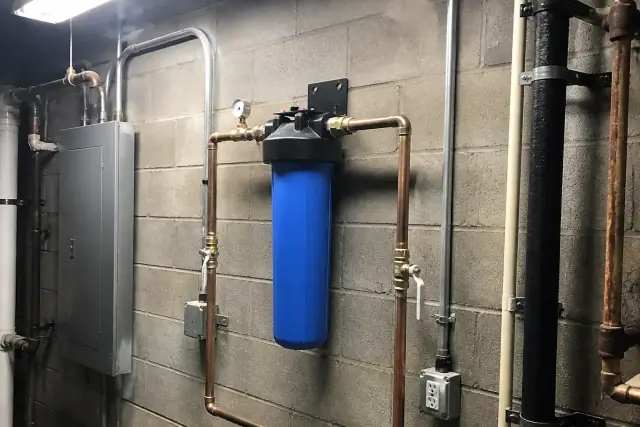 Blue sediment filter housing with copper piping mounted on a cinderblock wall in a Tempe, AZ mechanical room.