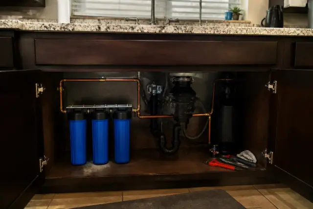 A whole house water filtration system with copper plumbing installed under a kitchen sink in a Tempe, AZ home.